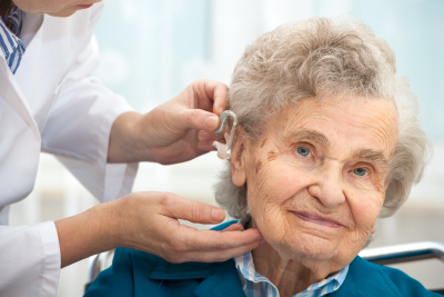 doctor inserting hearing aid in seniors woman ear