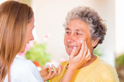 caregiver rubs the face cream on the senior woman face